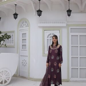 Model in a deep purple pure silk dress with full hand embroidery, stone and sequin embellishments, organza dupatta with four-sided stone lace, and matching pure silk trousers, standing in a white arched backdrop.