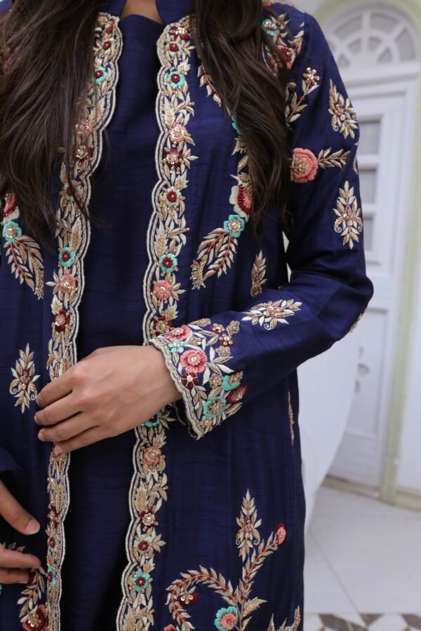 navy blue embroidered kurti with intricate multicolor floral patterns on the front panel, sleeves, and cuffs, worn by a woman.